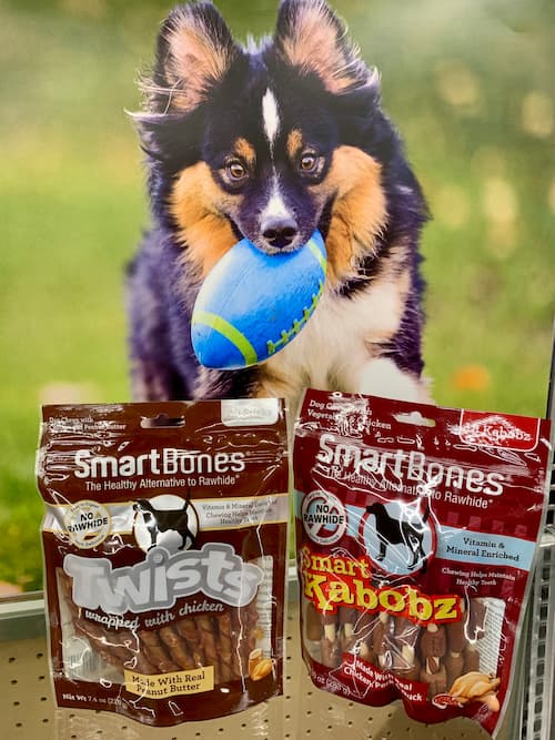 dog holding football in mouth with two bags of smartbones